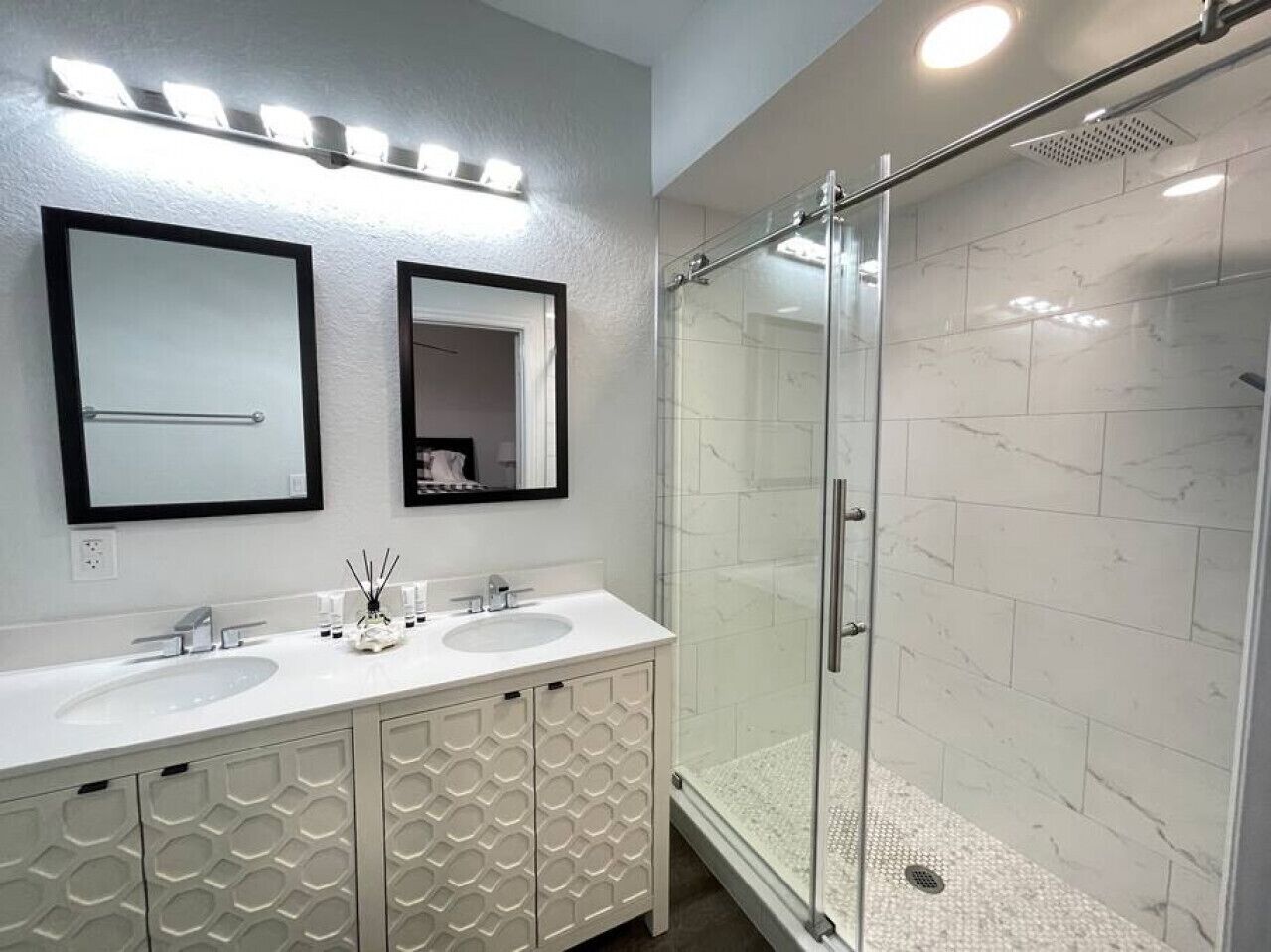 Un baño moderno con dos lavamanos, cabina de ducha de vidrio y un espejo grande sobre los lavamanos.