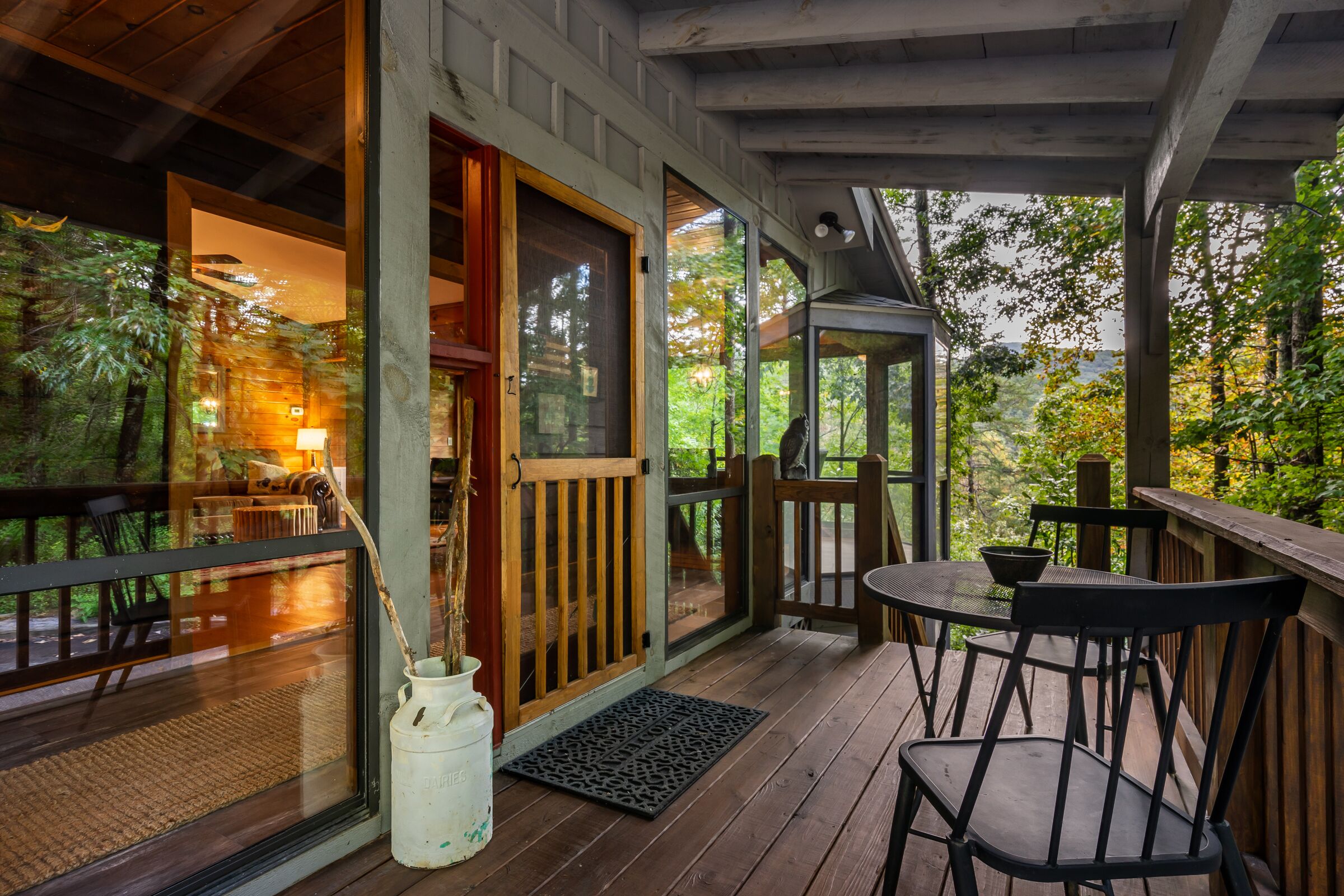 A wooden deck with a glass door leading to a room, a small table with chairs, and a potted plant.