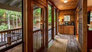 Une cabane en bois comprenant un coin repas, une cuisine et de grandes fenêtres donnant sur la forêt.