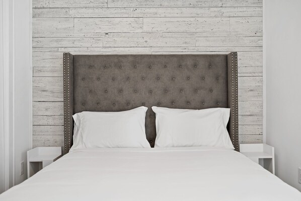A bed with a tufted headboard, two white pillows, and a white nightstand on either side.