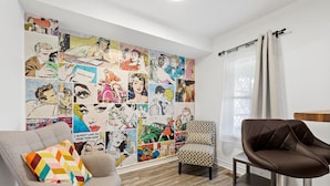 Une pièce dont un mur est décoré d’une fresque représentant des personnages de bandes dessinées, avec un tabouret de bar, un fauteuil rembourré et un coussin à motifs.