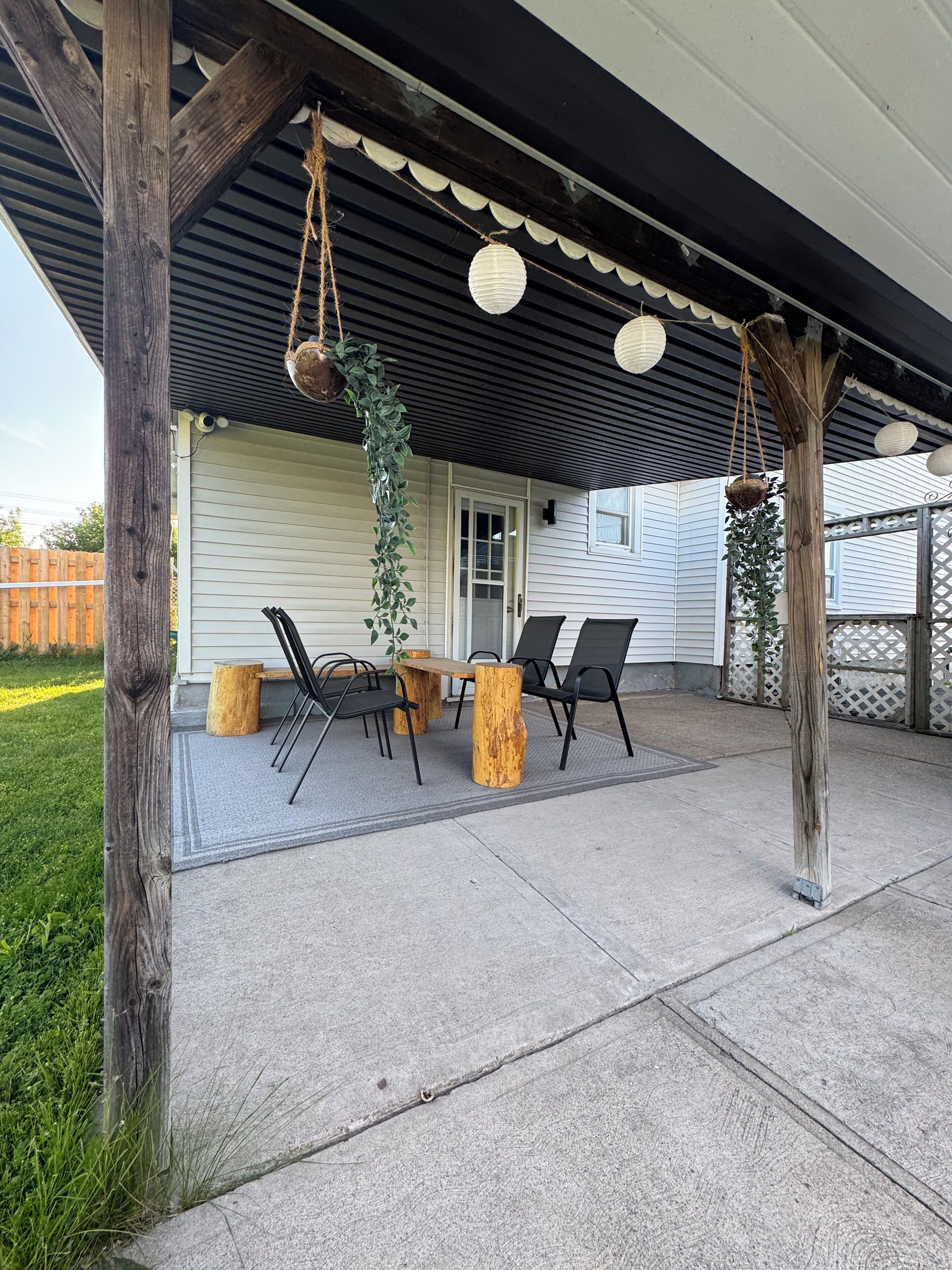 A covered patio area with a table and chairs, a hanging plant, and a wooden post.