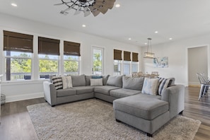 A spacious living room with a large sectional sofa, a ceiling fan, and large windows with blinds. - Waterfront Retreat! Fish, Boat & Relax (Bay St. Louis)