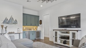 Un salon moderne avec un canapé gris, un téléviseur à écran plat et un coin cuisine doté de meubles de couleur turquoise.
