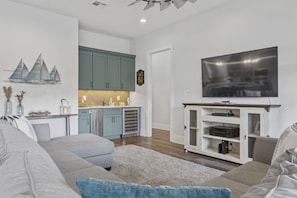 A modern living room with a grey sofa, a flat-screen TV, and a kitchen area with teal cabinets. - Waterfront Retreat! Fish, Boat & Relax (Bay St. Louis)