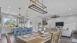 Une cuisine moderne dotée d’un îlot central, de tabourets de bar et d’un coin repas avec une table et des chaises en bois.