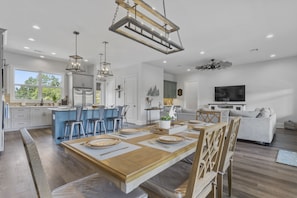 A modern kitchen with a central island, bar stools, and a dining area with a wooden table and chairs. - Waterfront Retreat! Fish, Boat & Relax (Bay St. Louis)