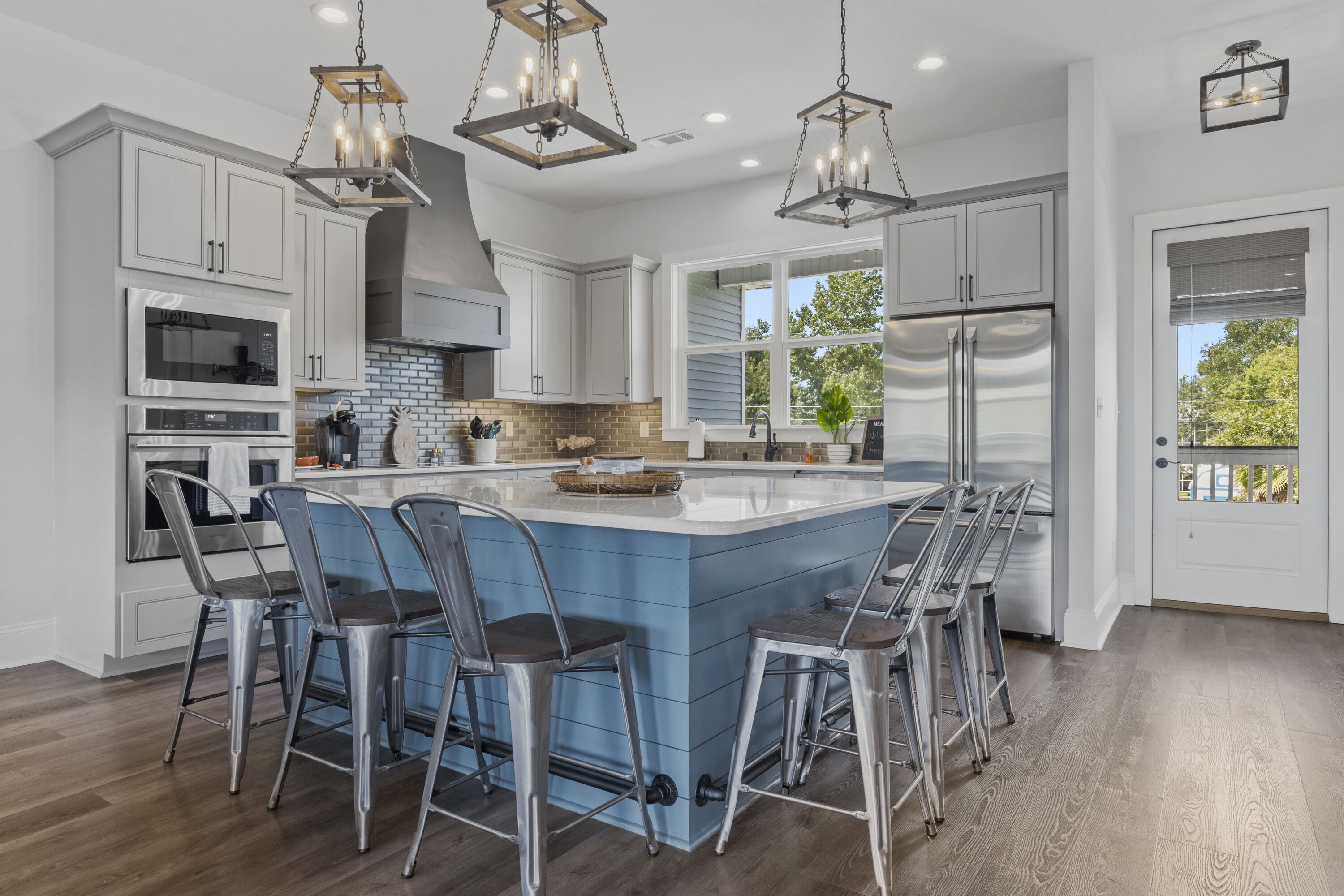 A modern kitchen with white cabinetry, a central island with bar stools, stainless steel appliances, and pendant lighting.