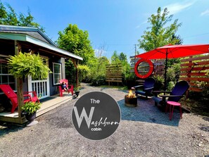 A cabin with outdoor seating, a fire pit, and a red umbrella.