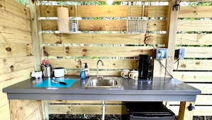 Une petite cuisine d’extérieur comprenant un évier, une machine à café et un réfrigérateur compact.