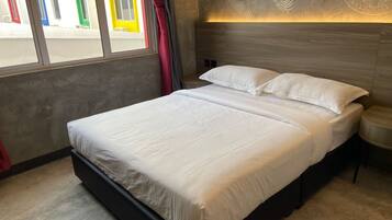Cama doble con sábanas blancas en una habitación moderna con pared de concreto y un diseño decorativo con hojas.