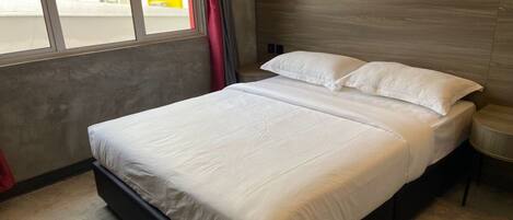Cama doble con sábanas blancas en una habitación moderna con pared de concreto y un diseño decorativo con hojas.