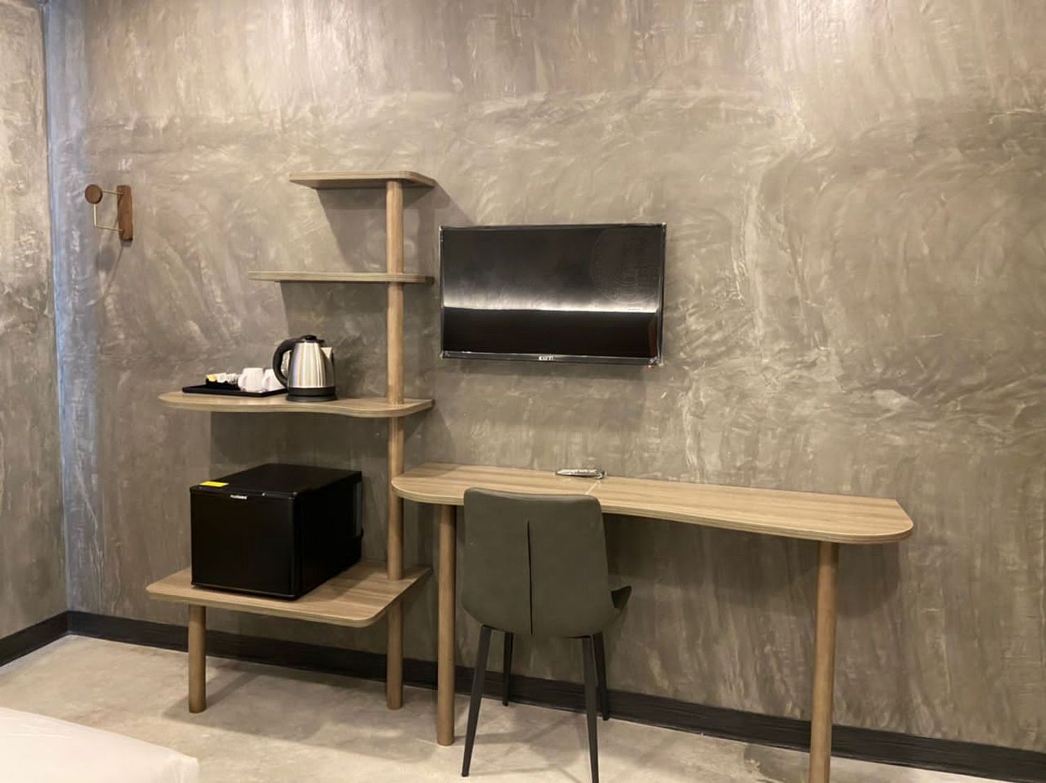 A modern room with a wooden desk, a chair, a TV mounted on the wall, and a shelf with a kettle and a box.
