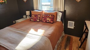 A bedroom with a large bed, two patterned pillows, a nightstand with a lamp, and a window with curtains. - Shady Rest in Hot Springs MT. (Hot Springs)