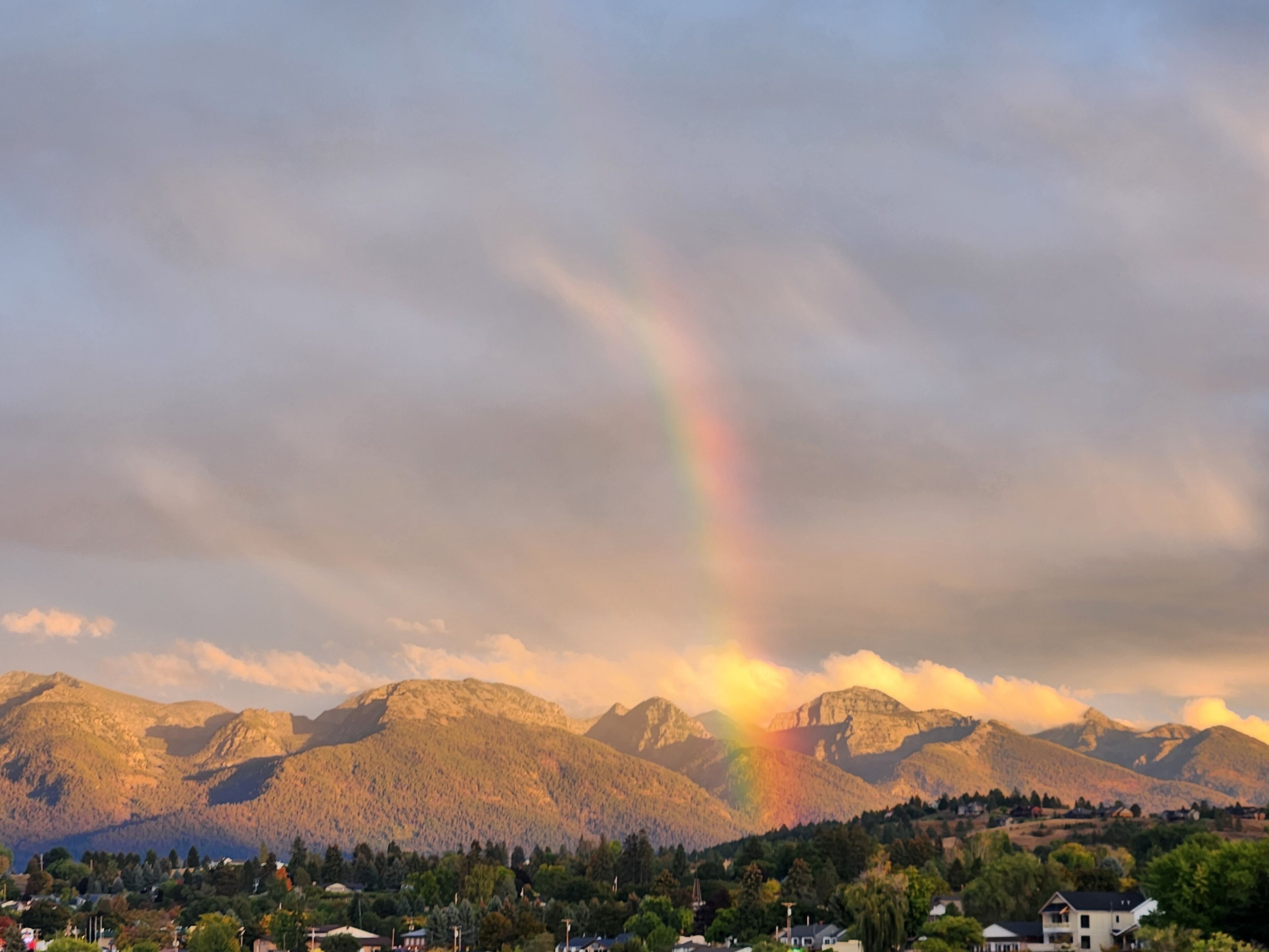 Un paysage de montagne avec un arc-en-ciel, des maisons et des arbres.