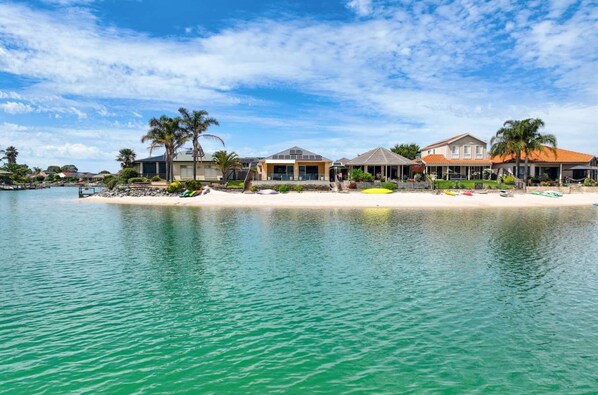 Une propriété située en bord de mer, comprenant plusieurs maisons, une plage de sable et une étendue d’eau calme.