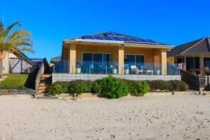 Une maison à deux étages avec un balcon, des panneaux solaires et une plage de sable au premier plan.