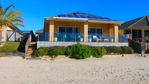 A beachfront house with a balcony, solar panels, and a sandy beach in the foreground.