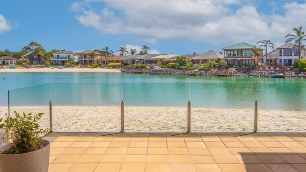 A beachfront property with a clear view of the sea, a sandy beach, and a row of houses with a rocky shoreline.
