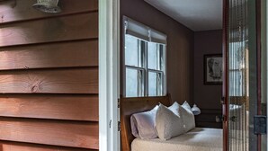 Un mur extérieur en bois avec une porte donnant sur une chambre. La chambre est équipée d’un lit avec des oreillers et d’une fenêtre.