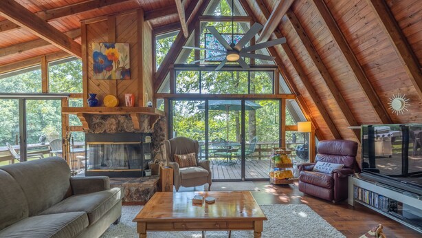 A spacious loft with a high ceiling, wooden beams, a fireplace, comfortable seating, and large windows offering a view of the outdoors. - The Foxtail Overlook by Innsbrook Vacations! (Innsbrook)