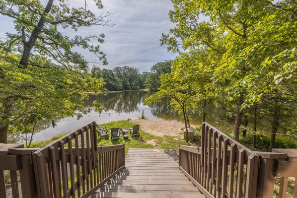 Une terrasse en bois qui mène à un lac, avec des chaises et une plage de sable.