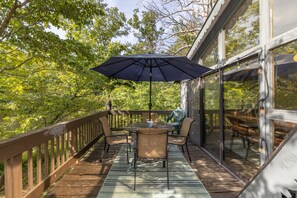 Une terrasse extérieure avec une table et des chaises, un grand parasol et une vue sur les arbres environnants.