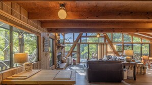 A spacious wooden interior with a large dining table, a sofa, and a view through large windows to the outdoors. - The Firefly Inn by Innsbrook Vacations! (Innsbrook)