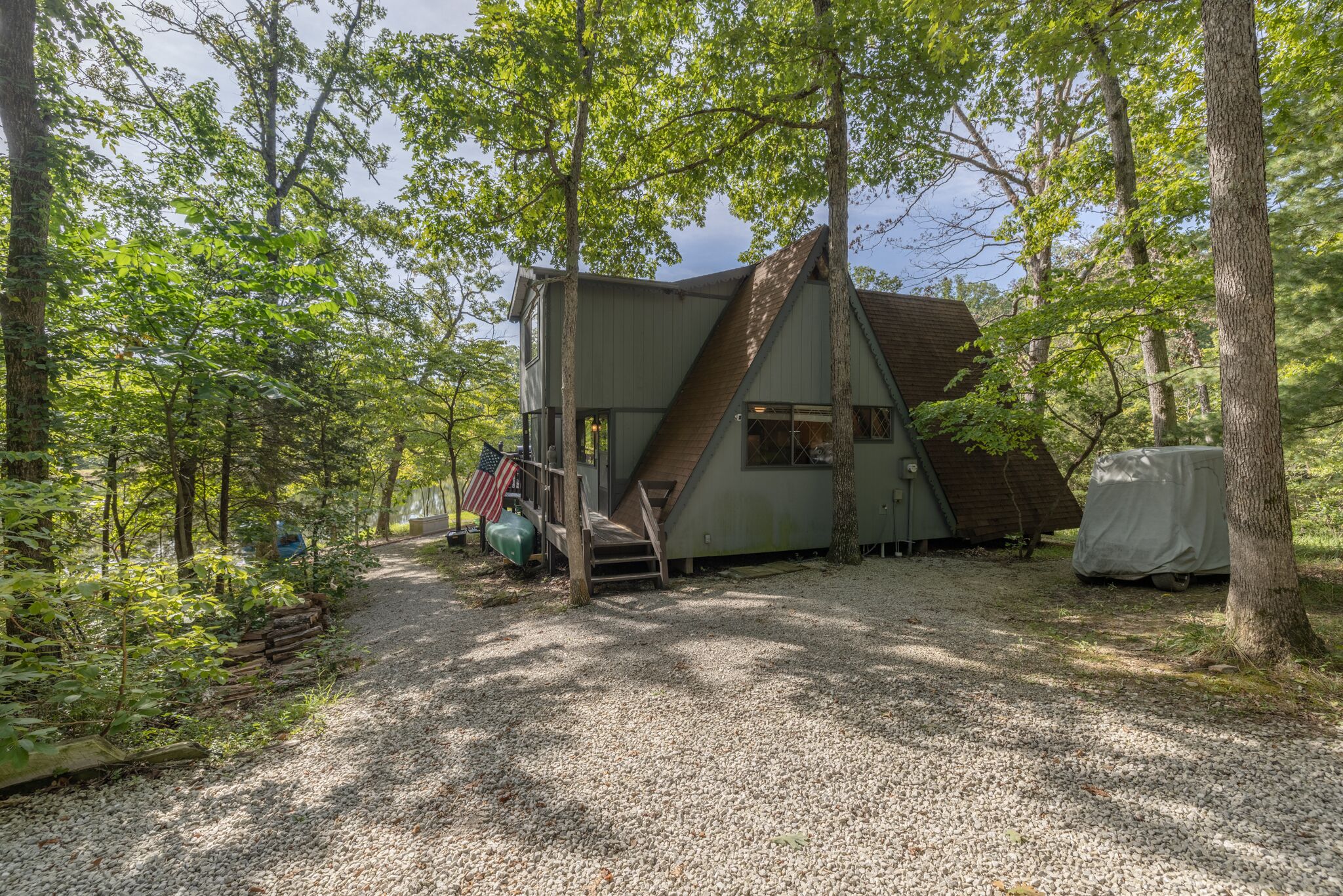 A cabin in a forest with a gravel path leading to it, surrounded by trees.