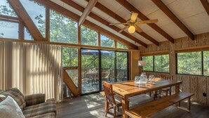 A spacious room with a wooden dining table, benches, and a sofa. Large windows provide natural light and views of the outdoors. - The Firefly Inn by Innsbrook Vacations! (Innsbrook)