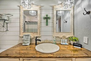 A bathroom with a wooden vanity, two mirrors, a sink, a towel rack, a cross, a plant, and a makeup bag. - Broken Bow Retreat w/ Large Yard + Fire Pit! (Broken Bow)