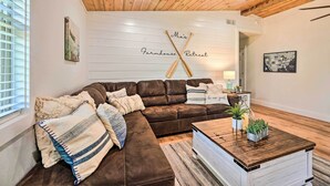 Ein gemütliches Wohnzimmer mit einem braunen Leder-Modulsessel, einem Holztisch und einer weißen Wand mit einem Schild mit der Aufschrift 'Farmhouse Retreat'.