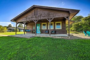 A rustic wooden building with a porch, a blue door, and a small seating area with chairs. - Broken Bow Retreat w/ Large Yard + Fire Pit! (Broken Bow)