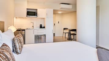 A modern hotel room with a large bed, a kitchenette, and a dining area.