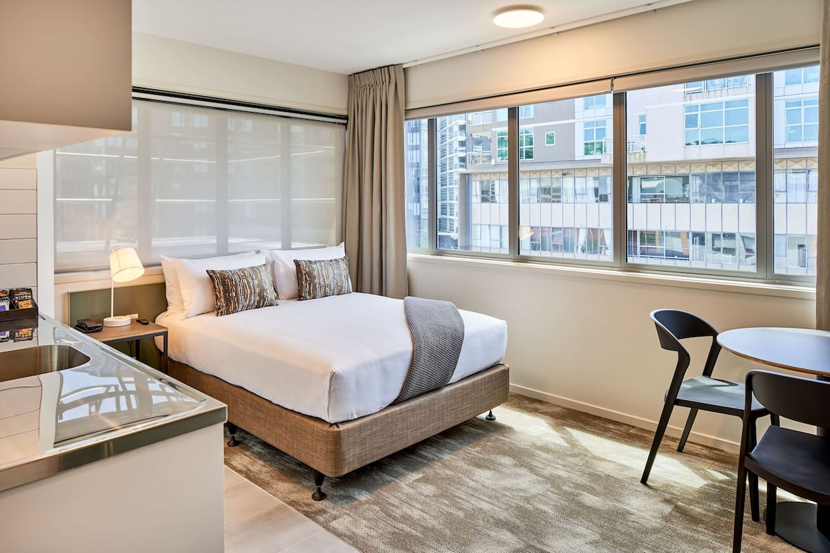 Une chambre d’hôtel avec un grand lit, un bureau et une chaise. Il y a une fenêtre donnant sur les bâtiments environnants.
