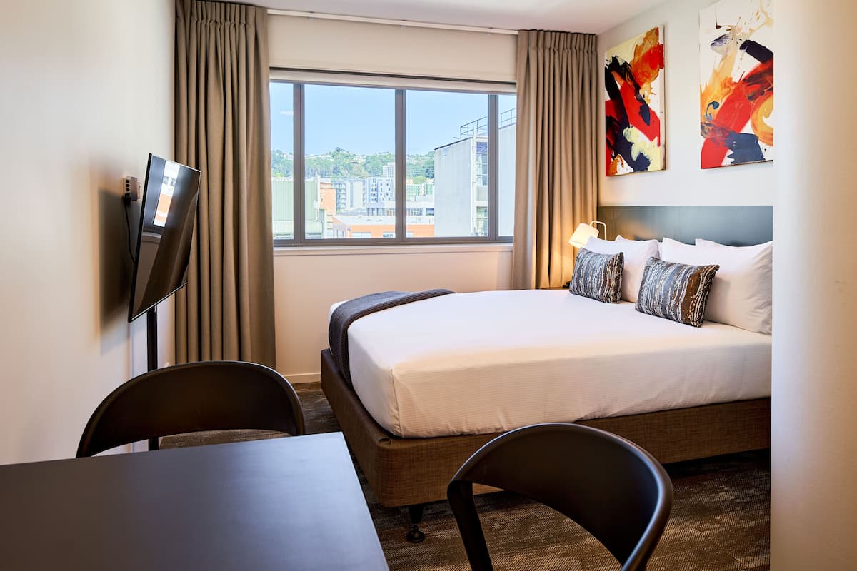 Une chambre d’hôtel équipée d’un lit, d’un bureau, d’une chaise, d’une télévision et d’une fenêtre avec des rideaux.