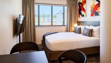 Habitación de hotel con cama, escritorio, silla, televisión y ventana con cortinas.