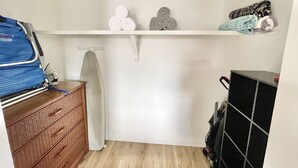 Una habitación compacta con un aparador de madera, una tabla de planchar y un estante con toallas dobladas y una manta.