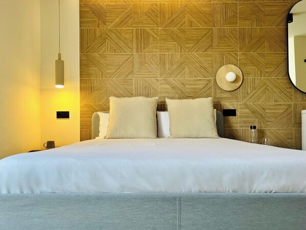 A hotel room with a large bed, a wooden patterned headboard, a round mirror, and a wall-mounted light fixture.