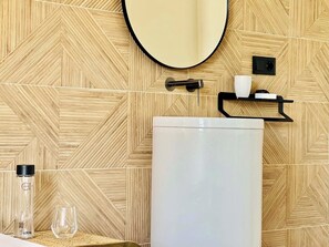 A bathroom with a large white sink, a mirror, and a wooden patterned wall. - Canaryislandshost l Mare (Puerto del Carmen)