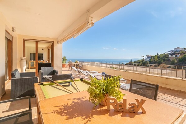 A balcony with a pool table, lounge chairs, and a view of the sea.