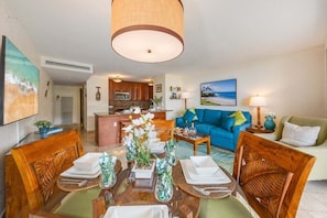 Un coin repas avec une table en bois dressée pour quatre personnes, un canapé bleu et une cuisine en arrière-plan.