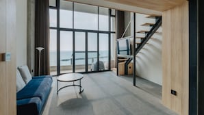 A modern room with a blue sofa, a round table, and a staircase leading to a balcony with a view of the sea.