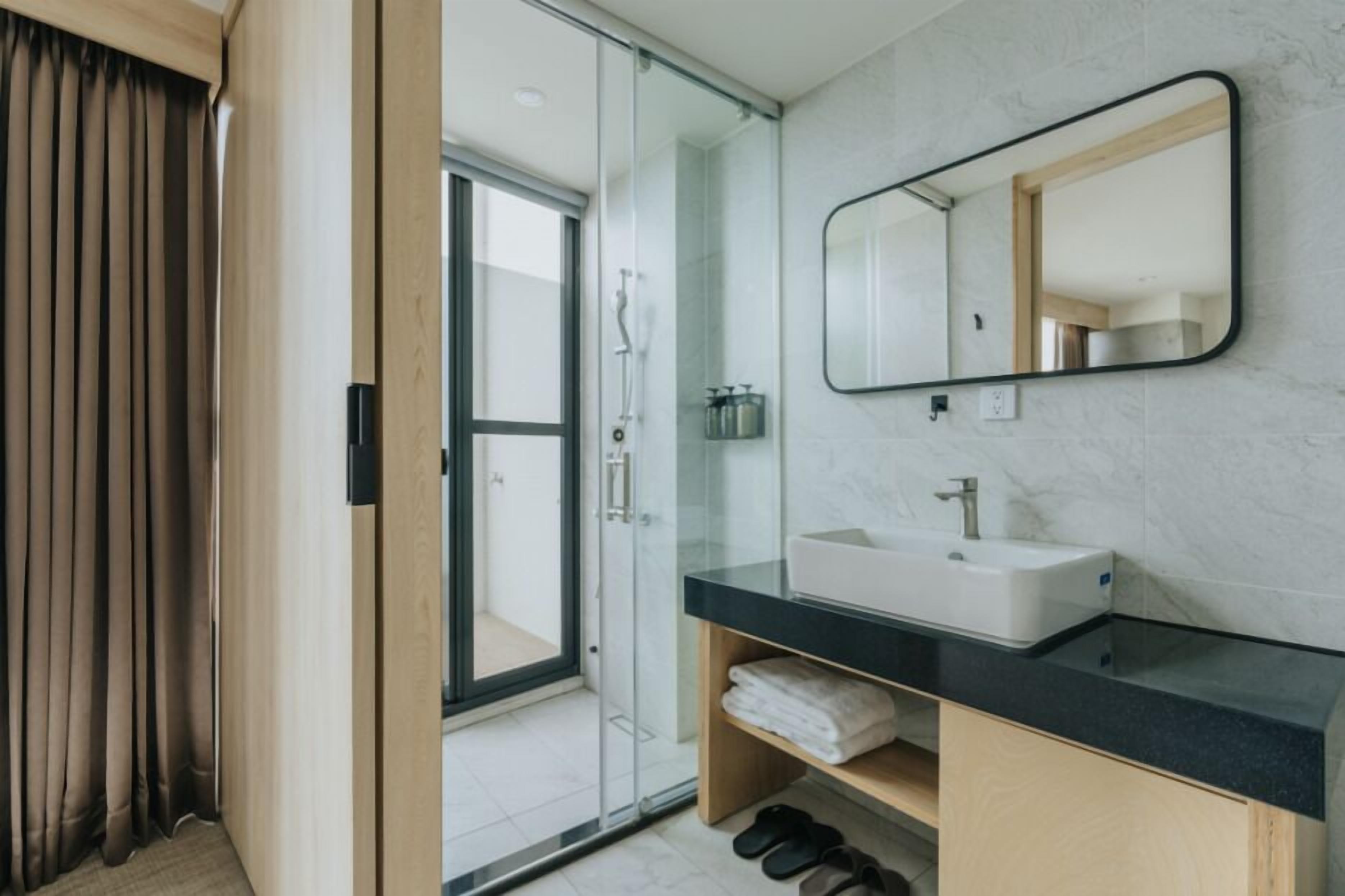 Un baño moderno con cabina de ducha de vidrio, un espejo grande y un lavabo blanco.