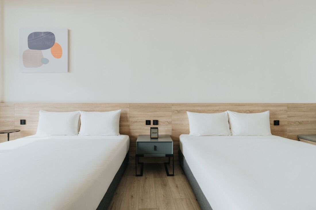 A hotel room with two beds, a nightstand, and a wall-mounted artwork.