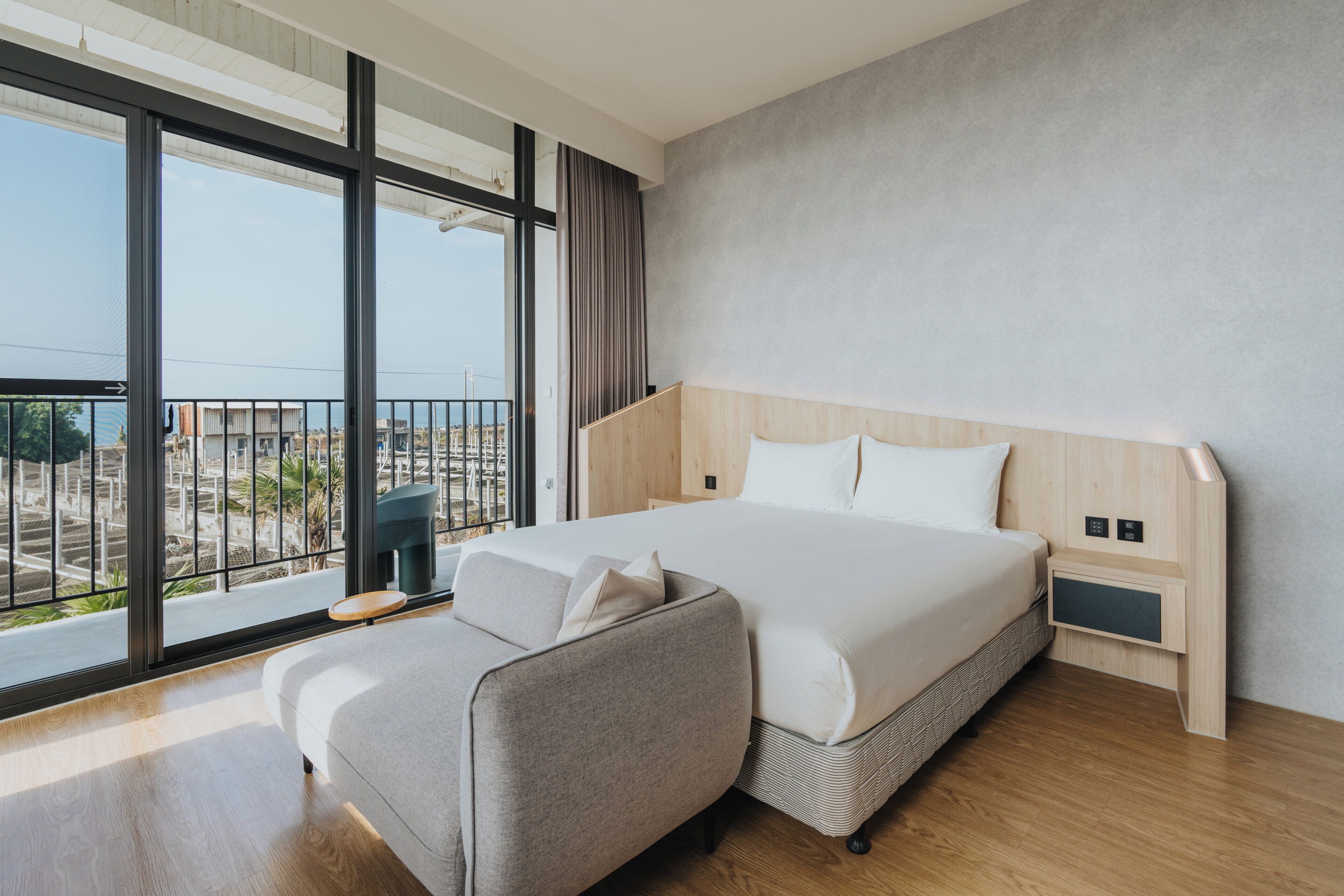 A modern hotel room with a large bed, a sofa, and a view of the city through large windows.