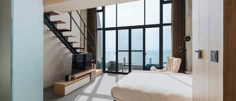 Un dormitorio moderno con una cama grande, televisión, una escalera y vista al mar.