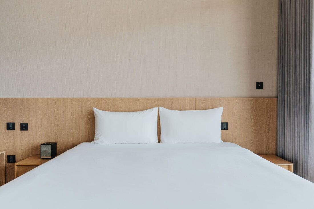 A hotel room with a large bed, wooden headboard, and a nightstand with a lamp.