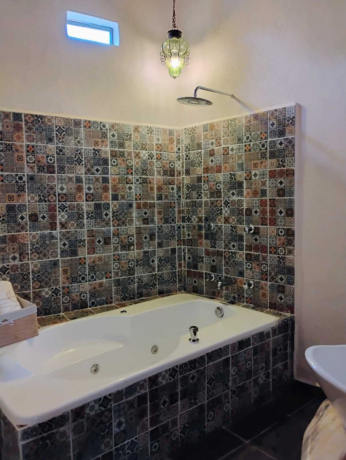 Baño con una bañera grande, ducha y lavabo. Las paredes están cubiertas de diversos diseños de azulejos.