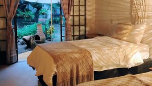 A cozy bedroom with a wooden ceiling, a large window with curtains, and a view of the garden outside.